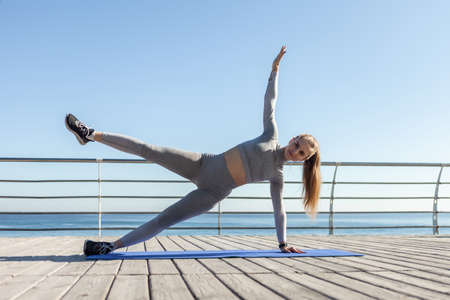 Young slim fit Caucasian woman practicing side plank on the beach. healthy lifestyle