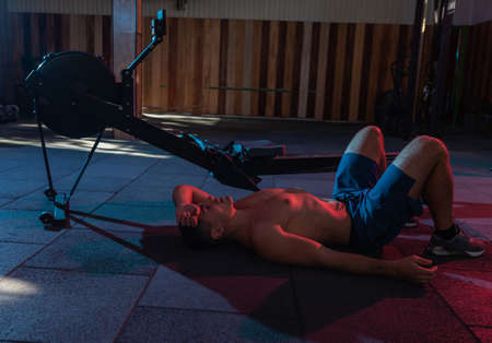 Tired exhausted male athlete lies on the floor in the gym in red blue neon light
