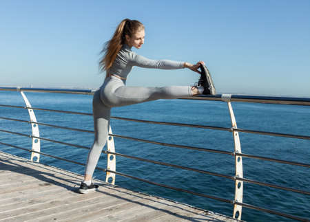 Fit woman in sportswear doing stretching leg on the beach at bright sunny day. healthy lifestyleの写真素材
