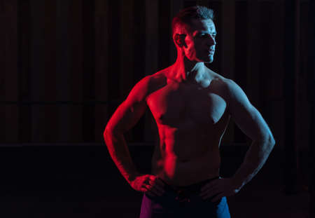 Athletic handsome man athlete with naked torso in red blue gradient neon light on black backgroundの写真素材