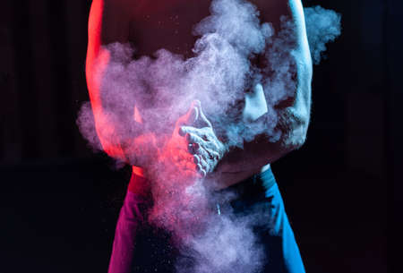 Weightlifter claps hands with talcum powder and prepares for workout in red blue gradient neon light.の写真素材