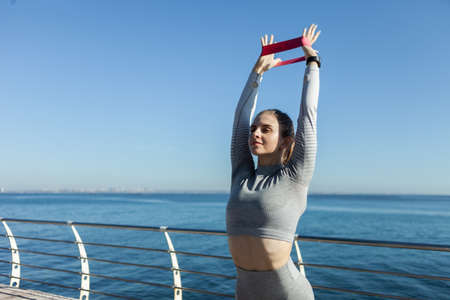 Young attractive caucasian fitness woman in sports clothes working out with fitness rubber bands on...