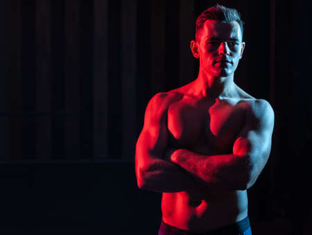 Athletic handsome man athlete with naked torso in red blue gradient neon light on black backgroundの写真素材