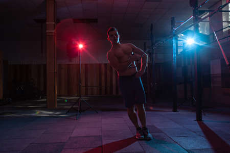 Muscular man works out with the trx system in a dark gym. Athlete with naked torso workout with...
