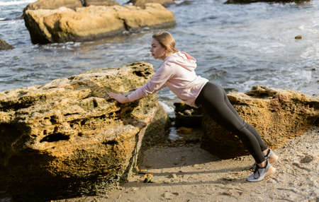 fitness woman push up from a stone on a wild beach on a bright sunny dayの写真素材