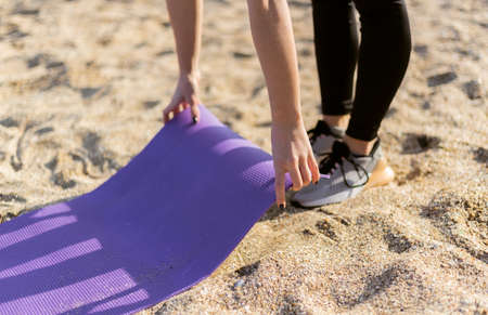 Woman unwinding mat on sand getting ready for workout or yoga on the beachの写真素材