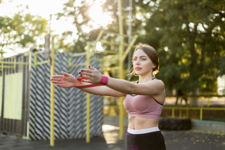 Fit slim woman trains hand with fitness rubber bands on sports ground