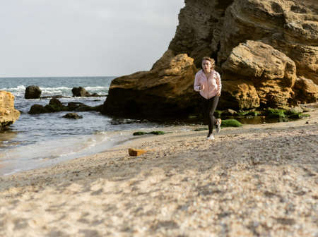 Fitness woman running on wild beach on bright sunny dayの写真素材