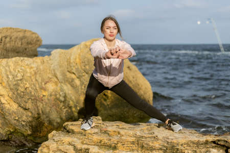 Young fitness woman works out her legs on the wild beach. healthy lifestyle