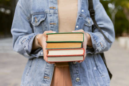 Student woman in stylish clothes holding stack of books outdoors