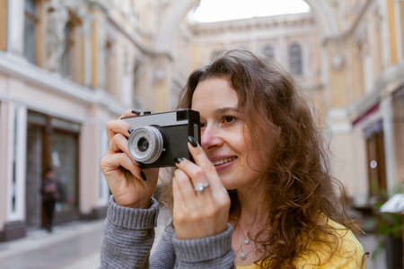 Cheerful curly hair woman tourist with retro camera in city. travel concept