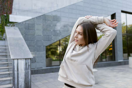 Fit brunette woman working out outdoors. Feminine sportswoman in sportswear practices stretching or...