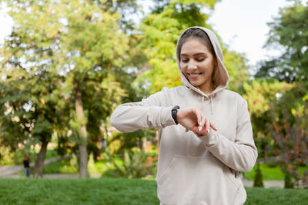 Fit runner woman in sportswear looks at smart bracelet measuring the pulse outdoor