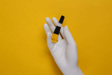 Mannequin's hand holds a tube of glue on a yellow background. top viewの写真素材