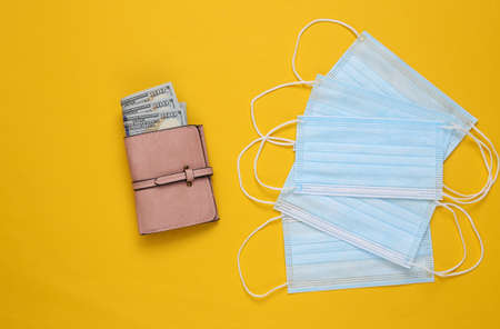 Medical masks and wallet with money on yellow background.