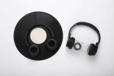 Two pairs of black stereo headphones, vinyl records and audio cassette on white background