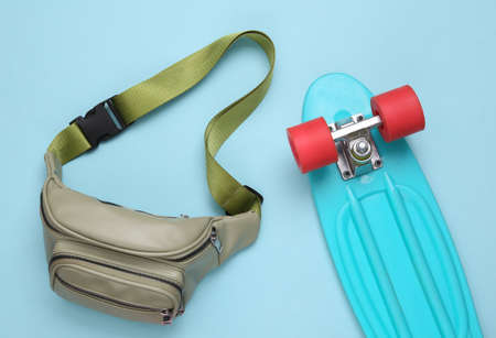 Waist banana bag, penny board on blue background. hipster outfit. top view