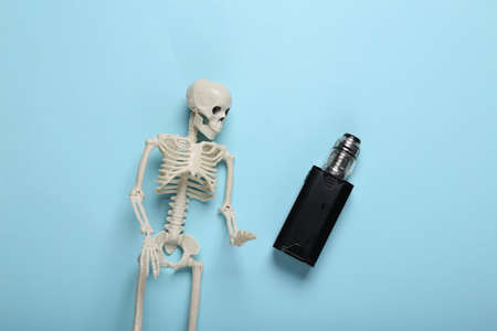 The harm of vaping. Skeleton and vaping device on a blue backgroundの写真素材
