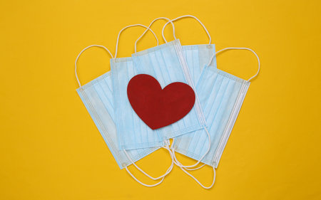 Medical facial masks and heart on yellow background. top viewの写真素材