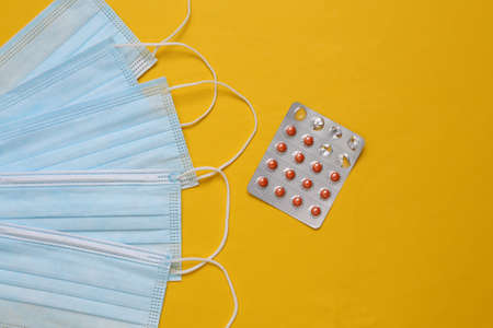 Medical facial masks and blister of pills on yellow background. top viewの写真素材