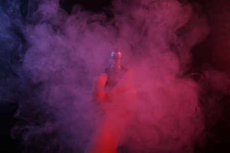 Hand holds an electronic cigarette or vaping device in dense smoke with pink blue neon light.の写真素材
