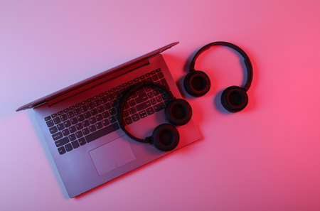 Laptop and Two pairs of wireless stereo headphones in red blue neon lightの写真素材