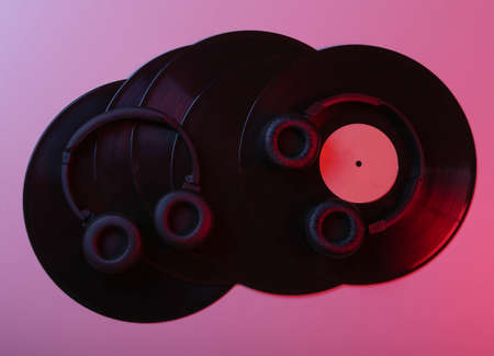 Two pairs of black stereo headphones and vinyl records in red blue neon light