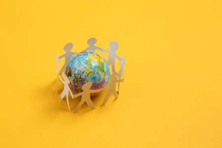 Cut paper human chain hold hands around the globe and show their unity on yellow background. solidarity and peaceの写真素材