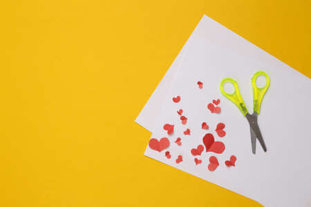 Handmade paper cut red hearts, scissors and paper on a yellow backgroundの写真素材