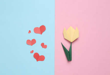 Handmade origami paper tulip and paper cut hearts on pink blue background. 8 March or mother's day...