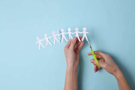 Female hands cutting paper chain from people on blue background