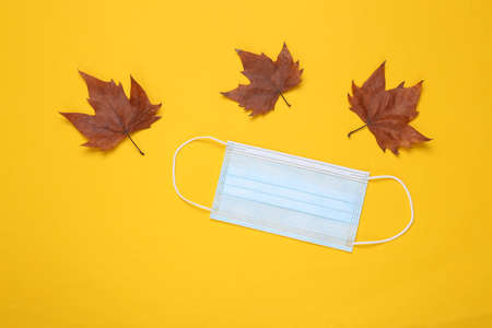 Medical mask and dry fallen leaves on yellow background.の写真素材