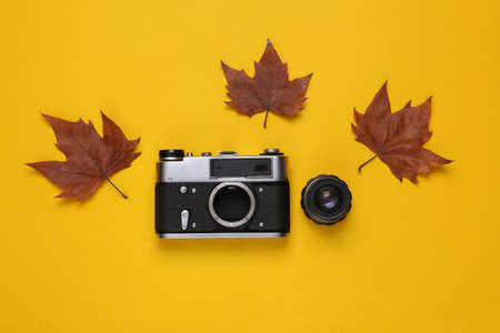 Vintage camera with lens and fallen leaves on a yellow background. top viewの写真素材