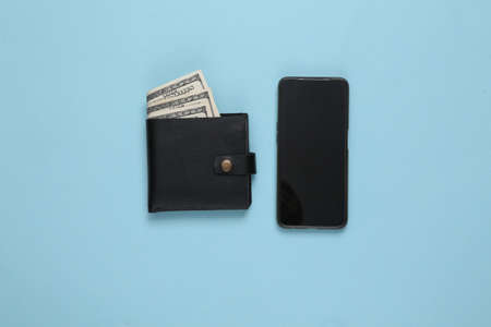 Leather wallet with one hundred dollar bills and smartphone on blue background. Online payments