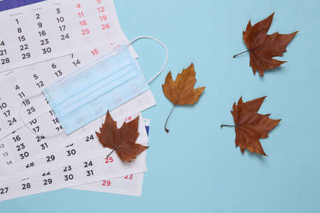 Calendar with fallen autumn leaves and a medical mask on a blue background. Autumn time. new reality. top viewの写真素材