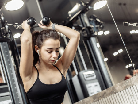 Young fit woman trains misci triceps in crossover exercise machine with ropes. Girl trains arms in modern gymの写真素材