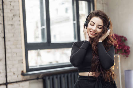 Cute young cheerful fit woman listens to music with headphones indoors.の写真素材