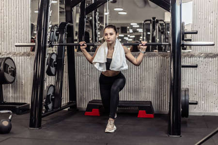 Attractive young fit woman trains leg muscles in barbell exercise machine in modern gym
