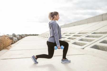 Fit slim sport woman trains leg muscles with dumbbells outdoors. healthy lifestyle. fitness, bodybuildingの写真素材