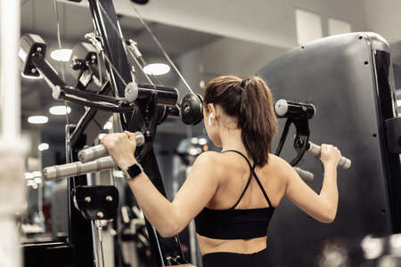 Young sporty woman exercising her back in lat exercise machine in modern gym