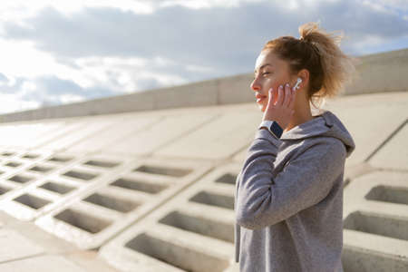 Attractive fit slim woman in sportswear listens to music in headphones outdoors