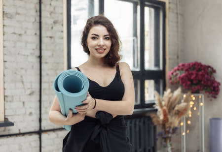 Fitness brunette woman holding yoga mat indoorsの写真素材