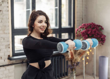 Attractive fit brunette woman trains muscles with dumbbells indoorsの写真素材