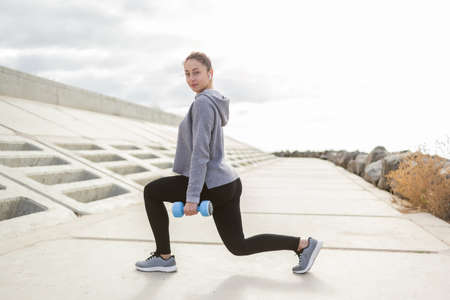 Fit slim sport woman trains leg muscles with dumbbells outdoors. healthy lifestyle. fitness, bodybuildingの写真素材