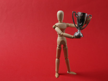 Wooden puppet holding the winner cup on red backgroundの写真素材