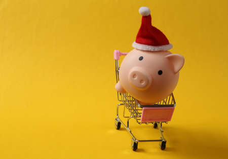 Piggy bank with santa hat, shopping trolley on yellow background. christmas shopping conceptの写真素材