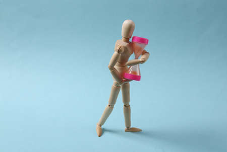 Wooden puppet holding hourglass on a blue backgroundの写真素材