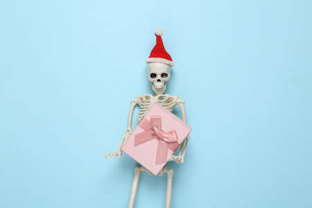 Skeleton with santa hat holding a gift box on a blue backgroundの写真素材