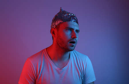 Pensive bearded Man in a foil hat in red-blue neon light.