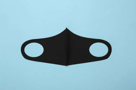 Black protective face mask on a light blue background. top view